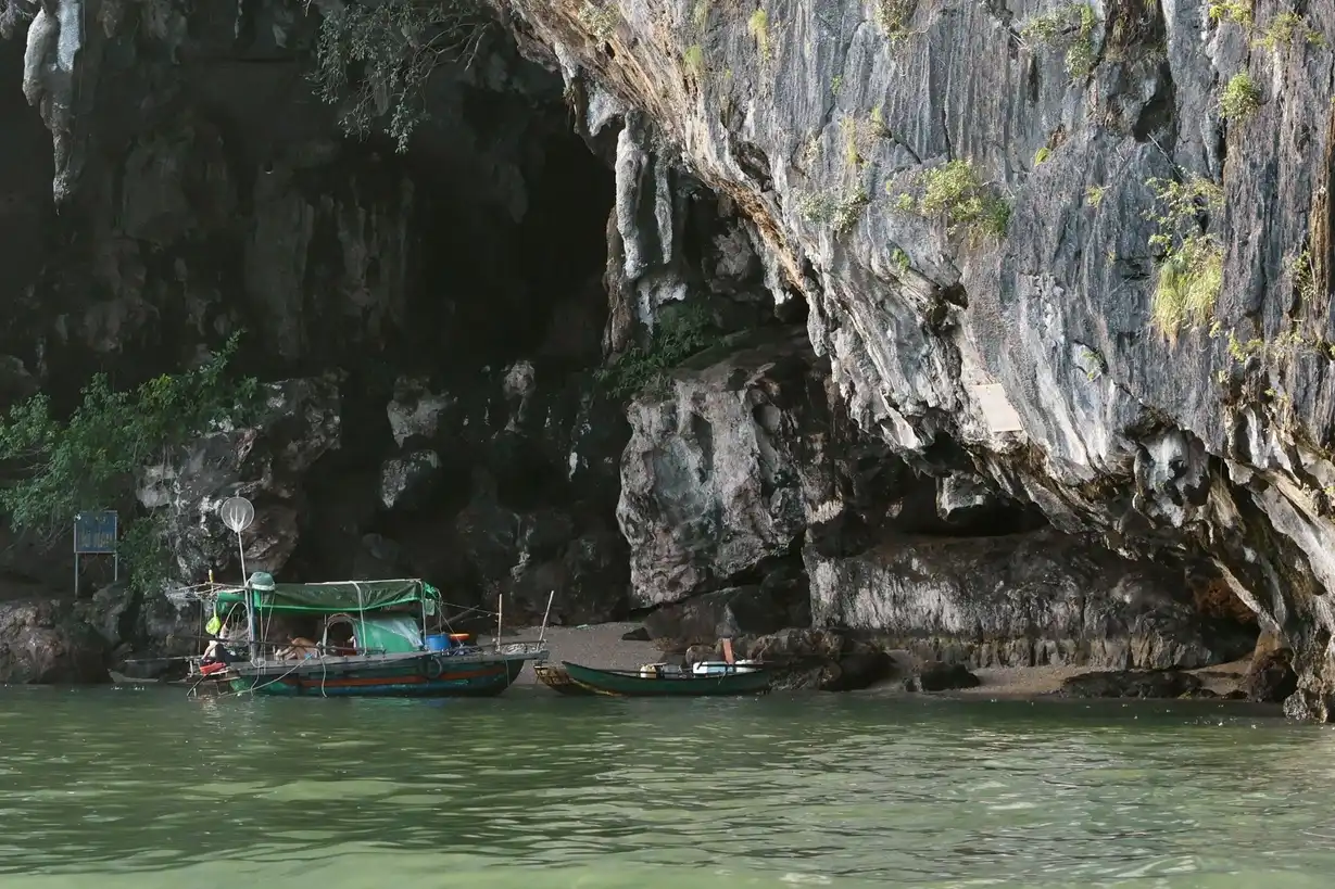 A small boat sheltered under a karst limestone formation in Ha Long Bay during a stormy weather.